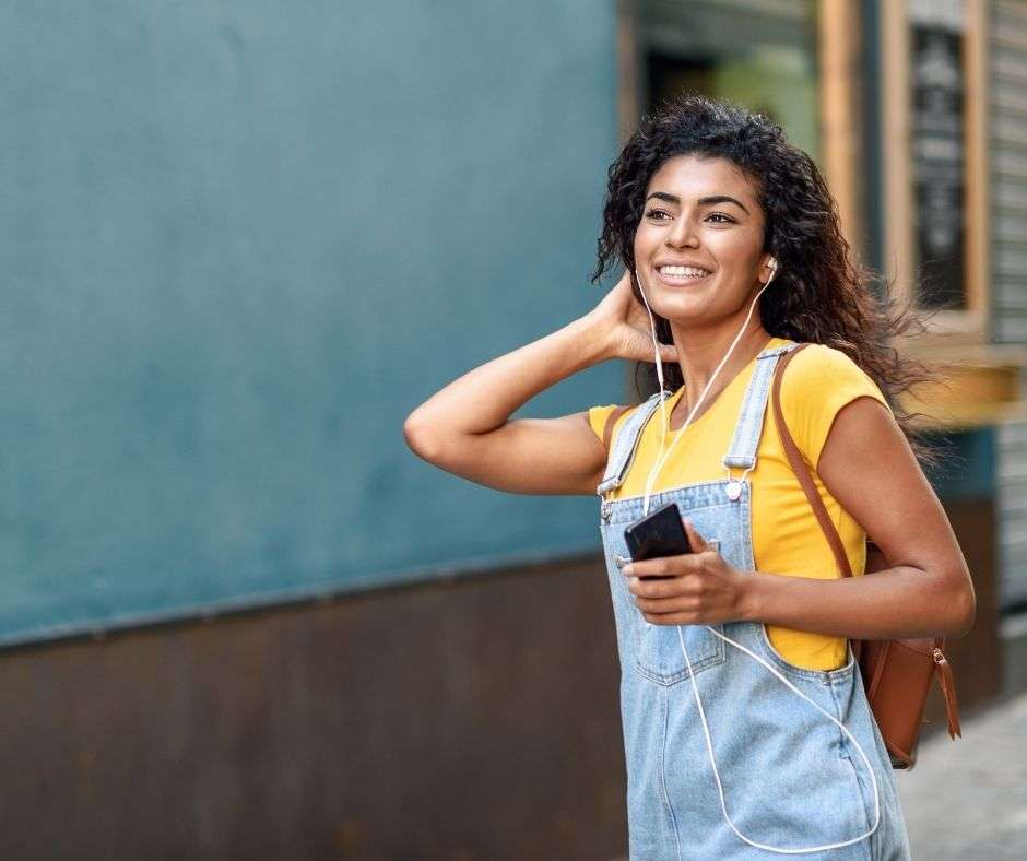 woman wearing yellow t-shirt and denim overalls listening to a podcast